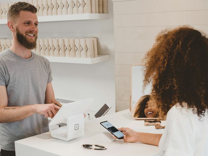 Un commerçant souriant encaisse une cliente au comptoir de sa boutique