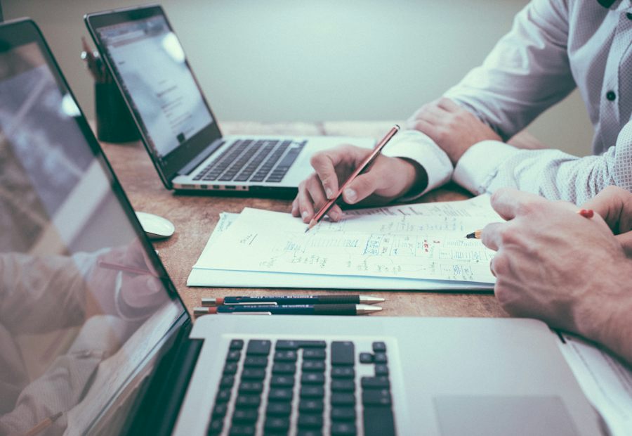 Deux personnes annotent un document financier entre deux ordinateurs