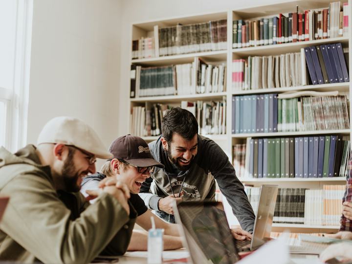 Trois étudiants rient ensemble devant un ordinateur dans une bibliothèque