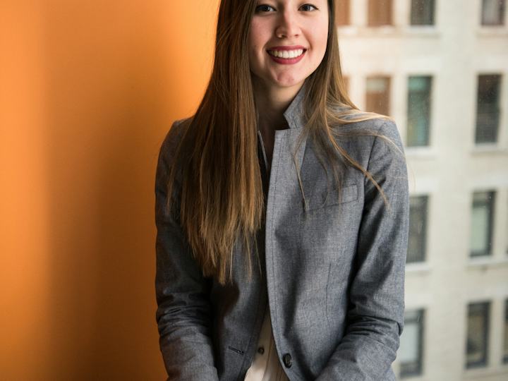 Jeune femme souriante en veste grise devant une fenêtre de bureau